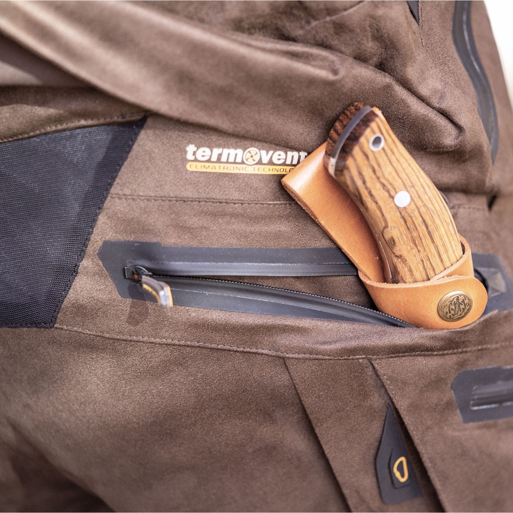 In der Reißverschlusstasche der Hillman 6OL Winter-Jagdhose steckt ein Messer mit Holzgriff. Die Hose ist mit einem „Termovent“-Etikett mit „Clima Tecno Technology“ versehen und eignet sich perfekt für Wanderungen bei kaltem Wetter.